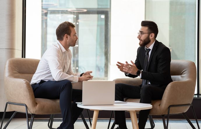 Middle eastern and caucasian ethnicity businessmen seated on armchair in modern office talking solve common issues, banker telling to client regarding bank services make recommendations and consulting